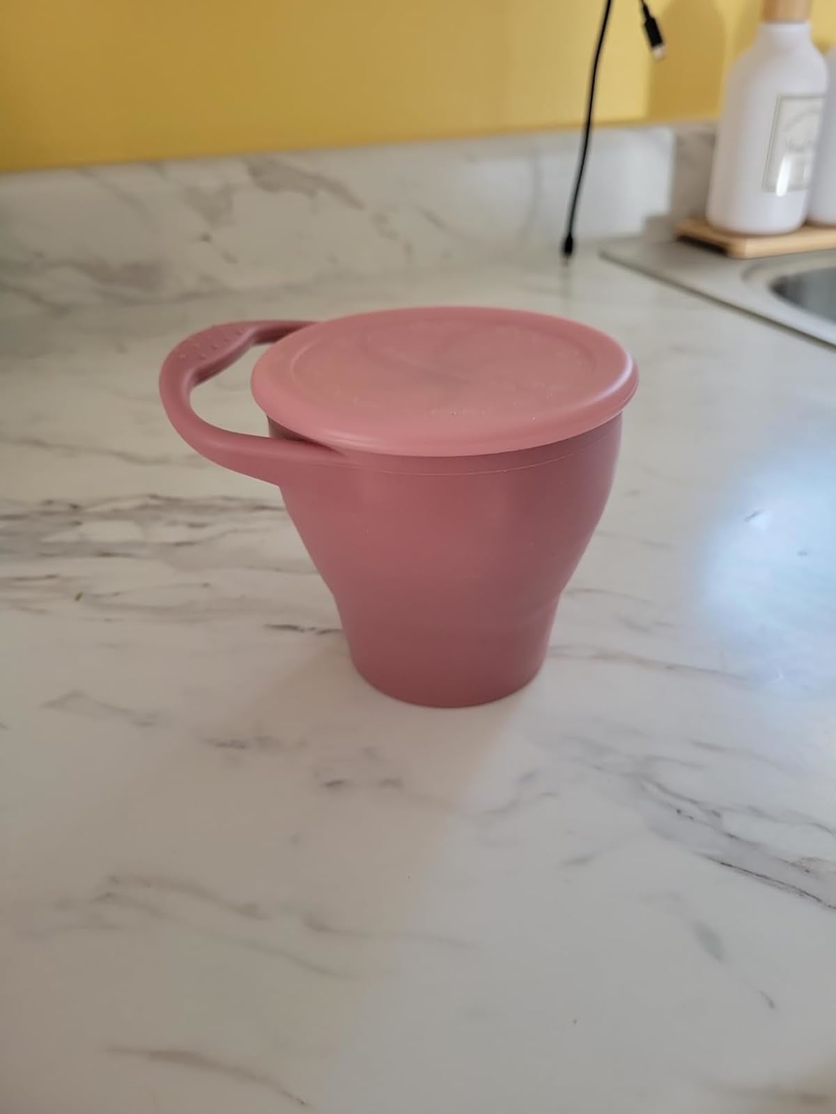 A collapsible silicone cupful  with lid connected  a room  counter, illustrating an eco-friendly, space-saving design