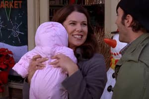 Two people from a TV show, one holding a baby, smiling at each other outside a market