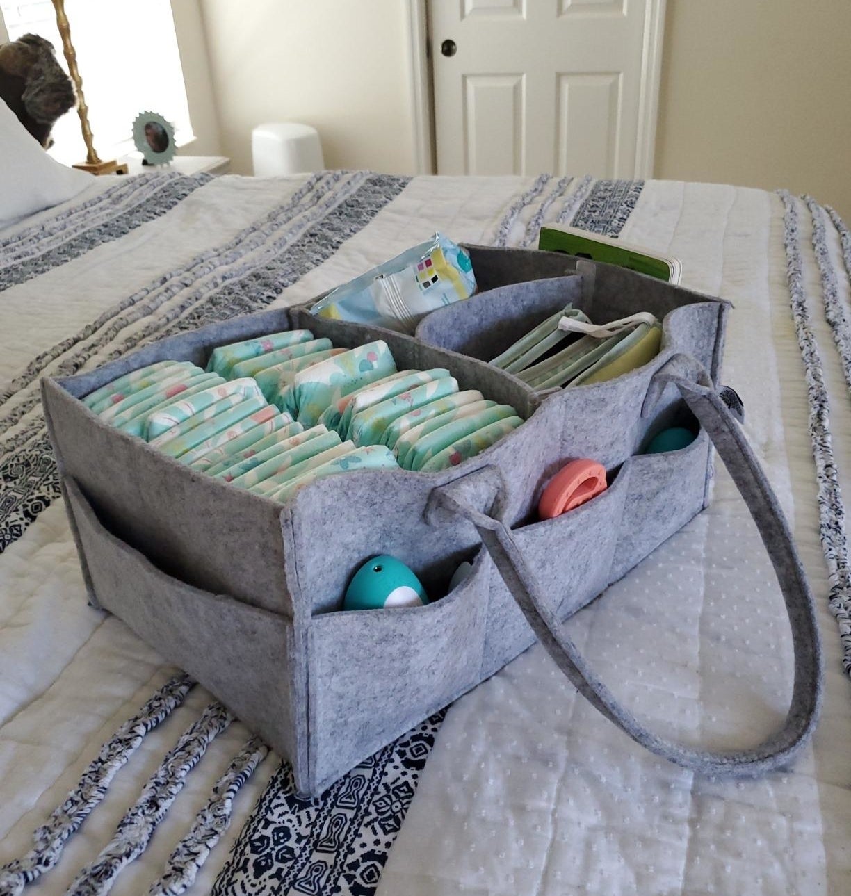 Foldable diaper caddy organizer with compartments, stocked with baby supplies on a bed