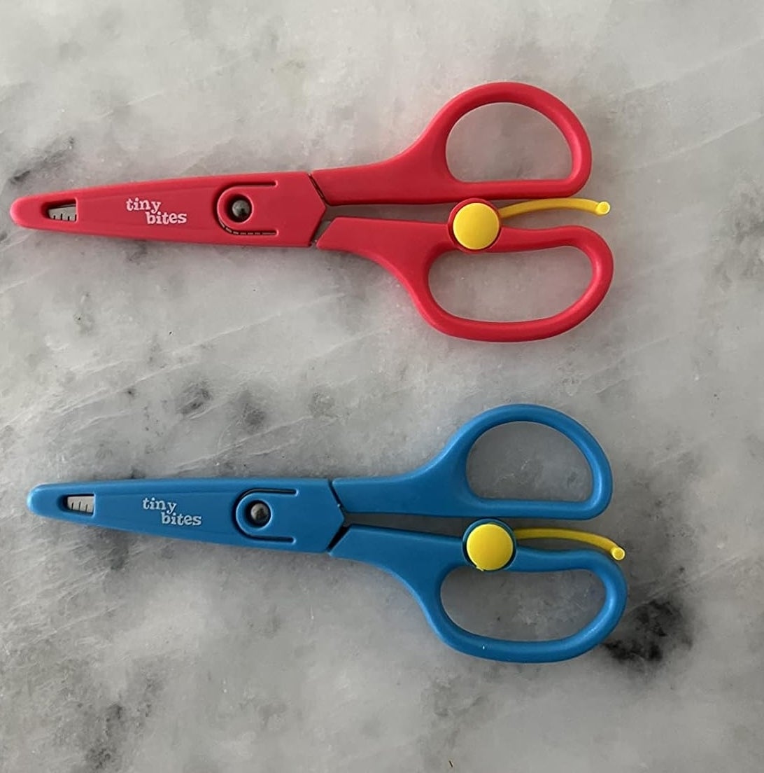 Two pairs of child-friendly scissors with circular handles, one red and one blue, on a marble surface