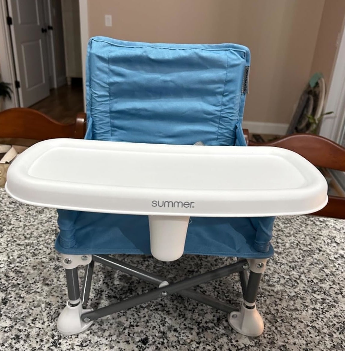 Blue portable child&#x27;s booster seat with a white tray by Summer Infant on a countertop
