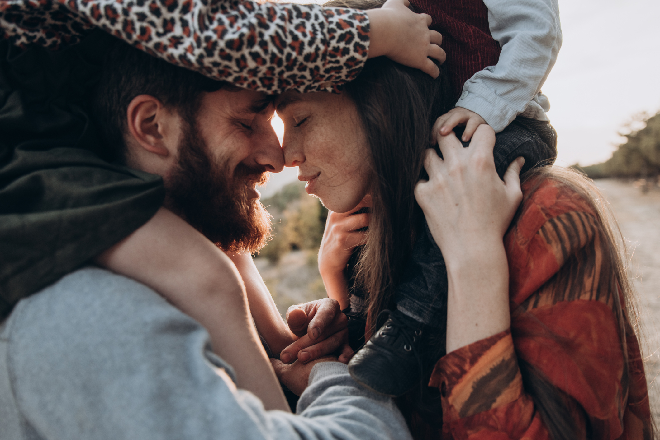 Parents holding a child, about to kiss, showing affection in a natural setting