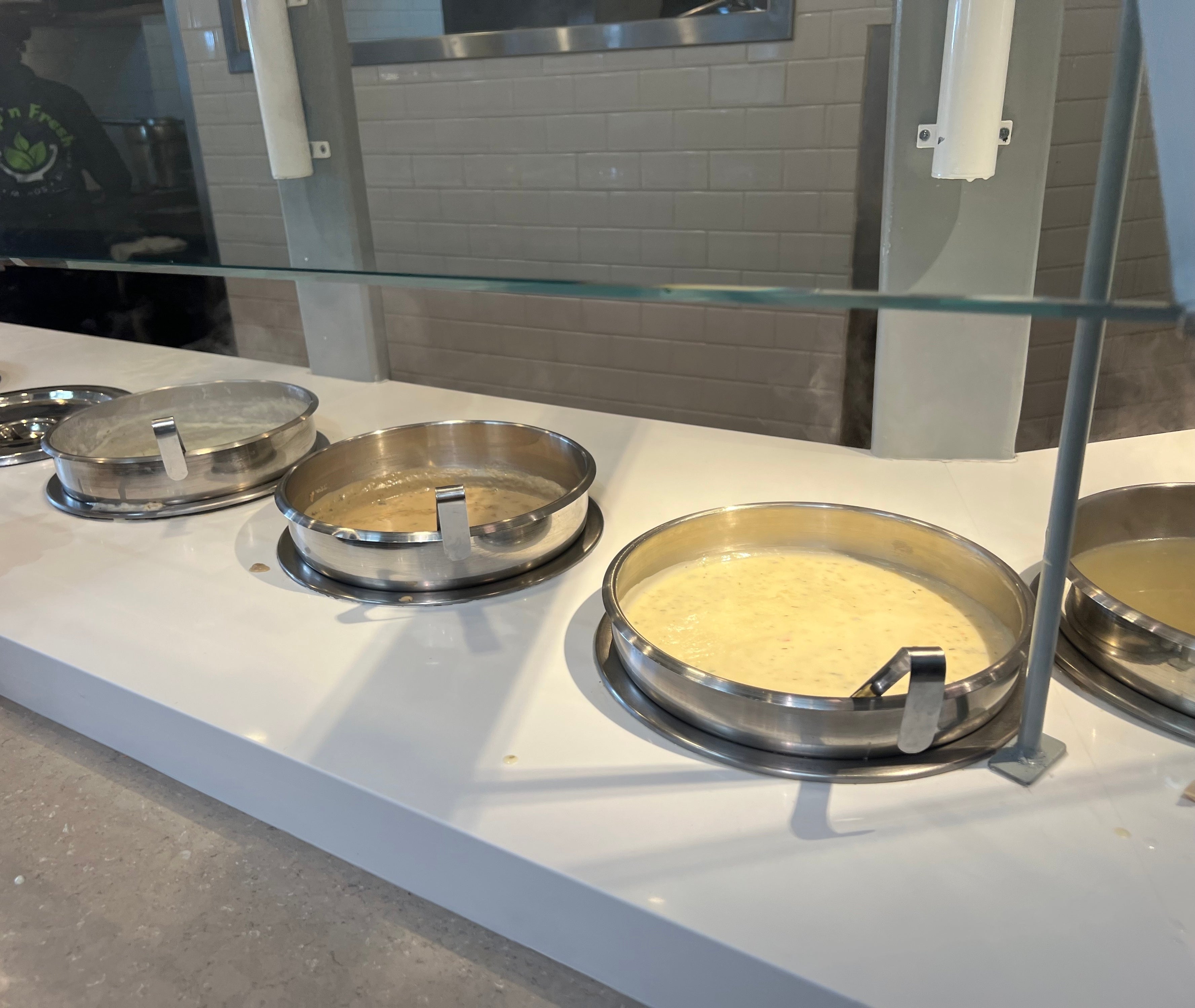 A cafeteria line with open containers of food and a person's hand visible