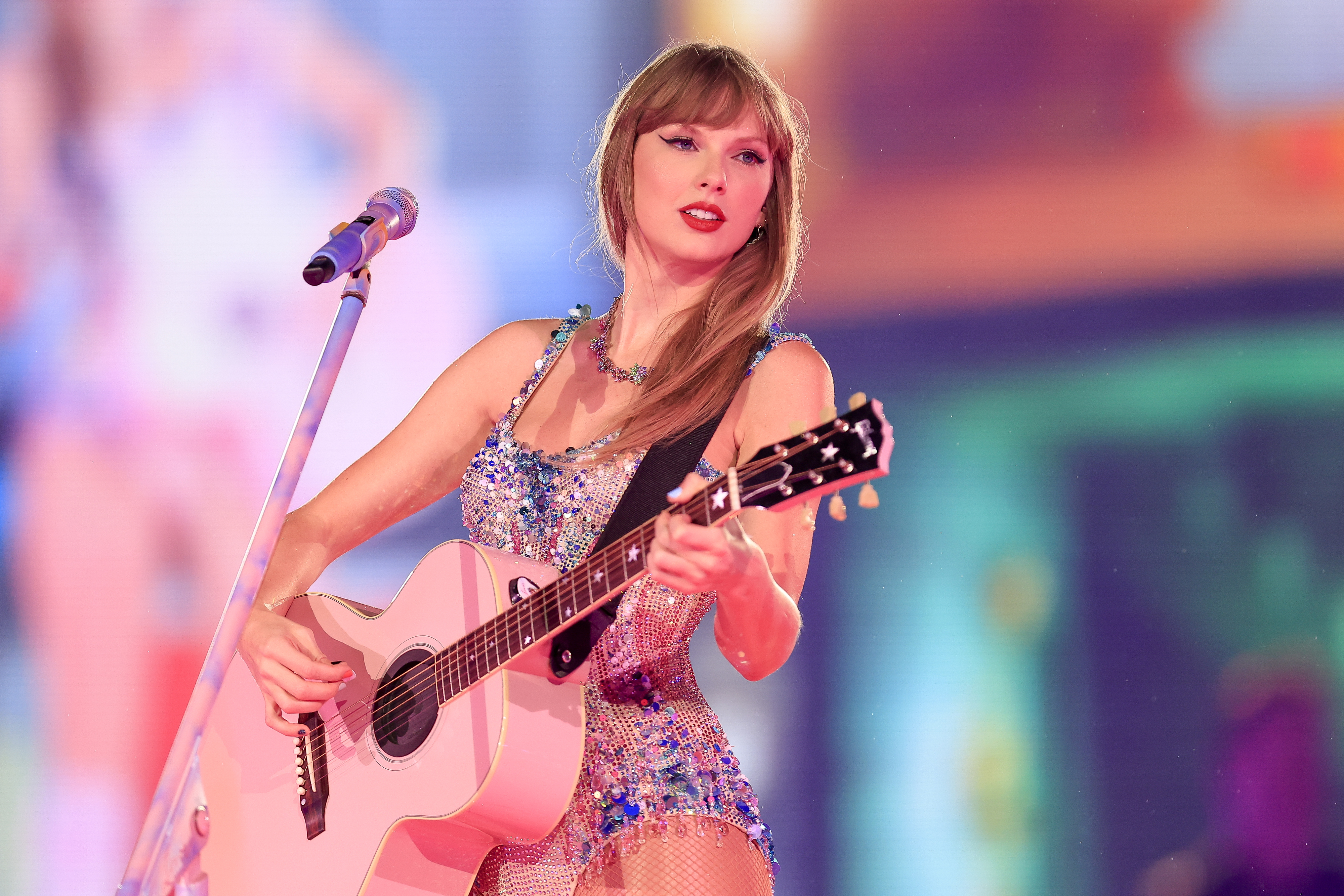 Taylor Swift performing with a guitar, wearing a sparkling dress