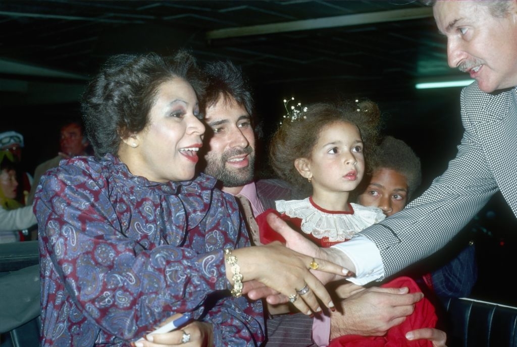 Minnie Riperton shaking a fan&#x27;s hand while Richard Rudolph holds Maya, and Marc Rudolph is in the background