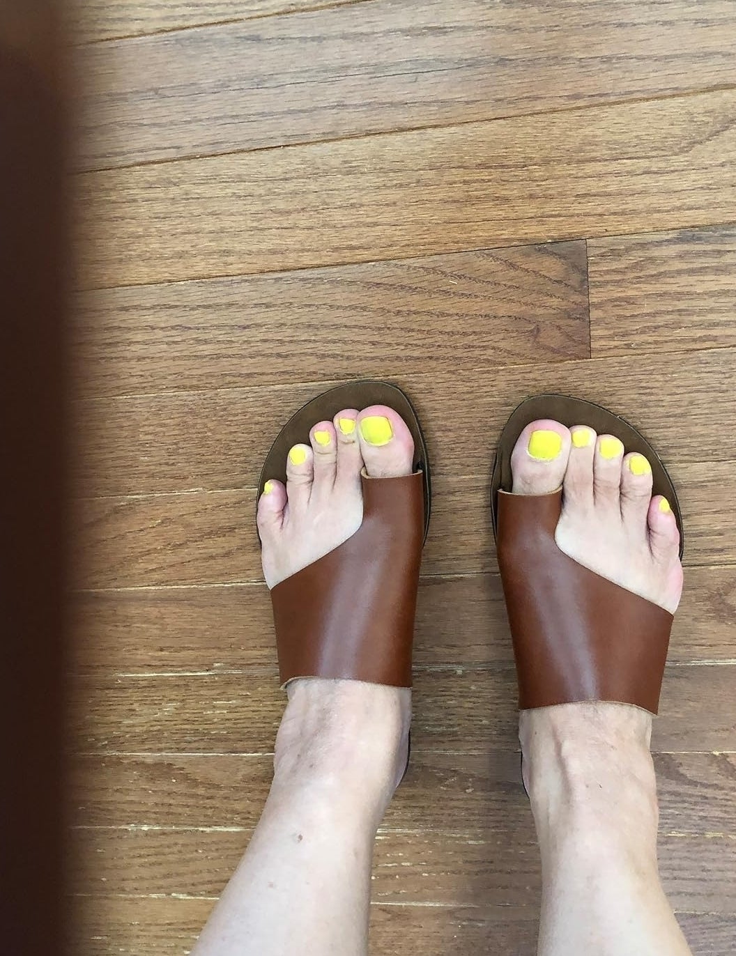 Person wearing brown slide sandals with bright yellow toenail polish