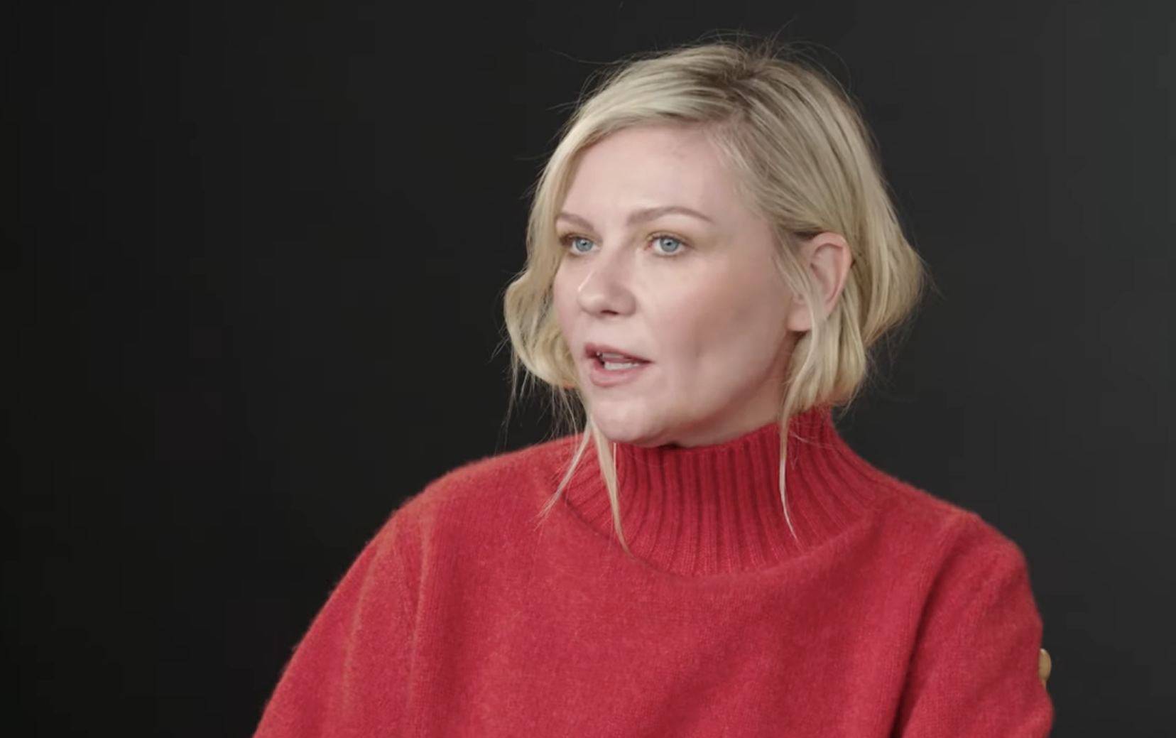 Kristen Dunst in red top speaks in a video titled &quot;Kristen Dunst Breaks Down Her Most Iconic Characters&quot; on YouTube