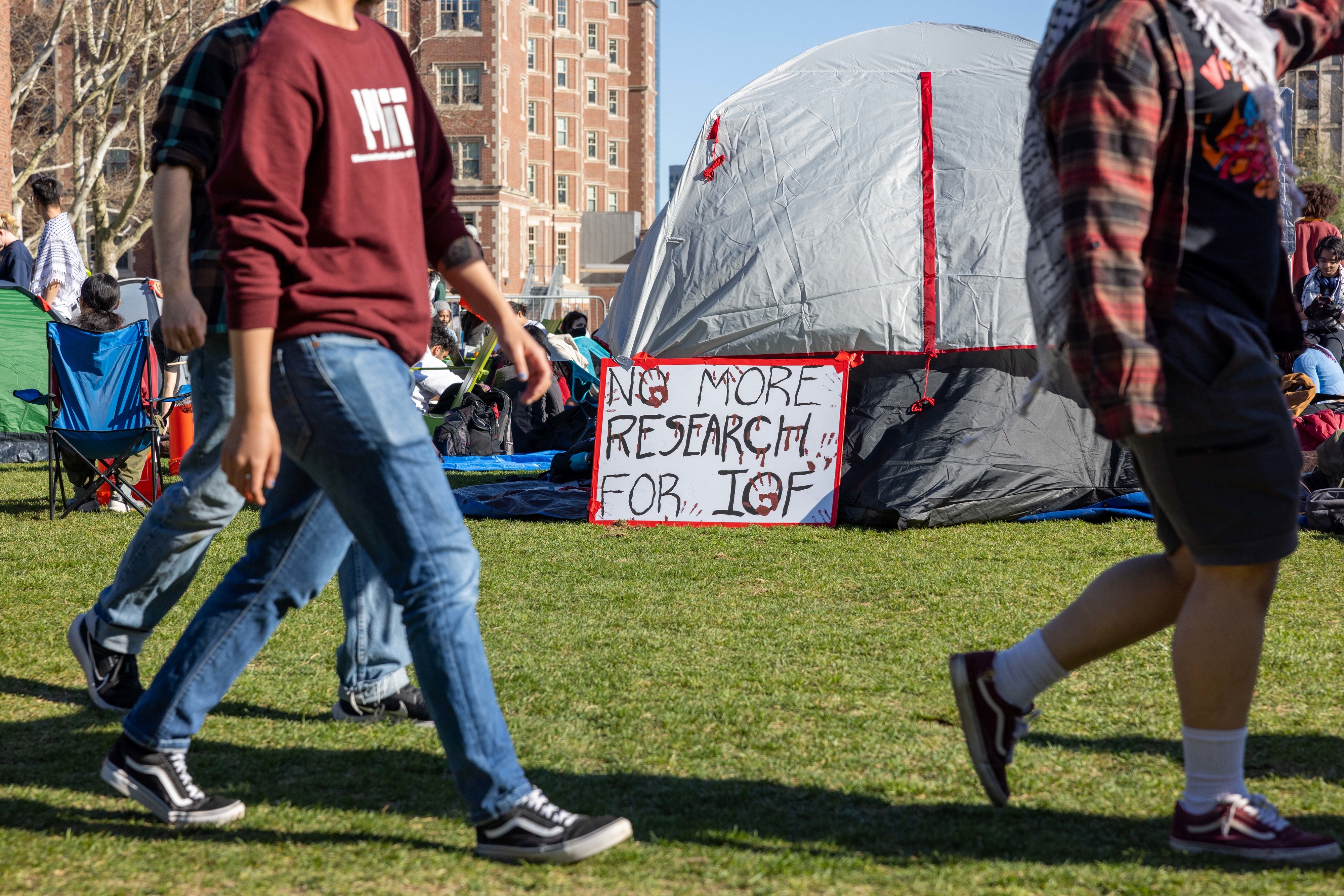 Protest sign reading &quot;No More Research for IGF&quot; in front of a tent with people passing by