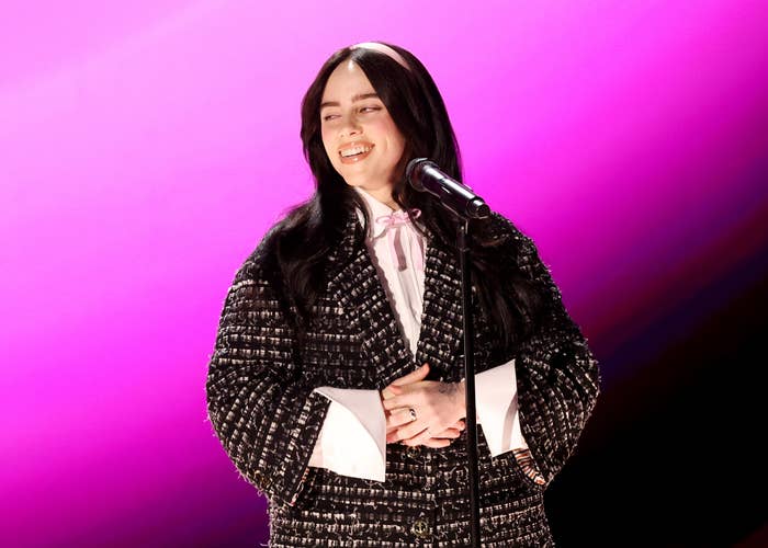 Billie Eilish on stage smiling in a textured black jacket and a bow tie
