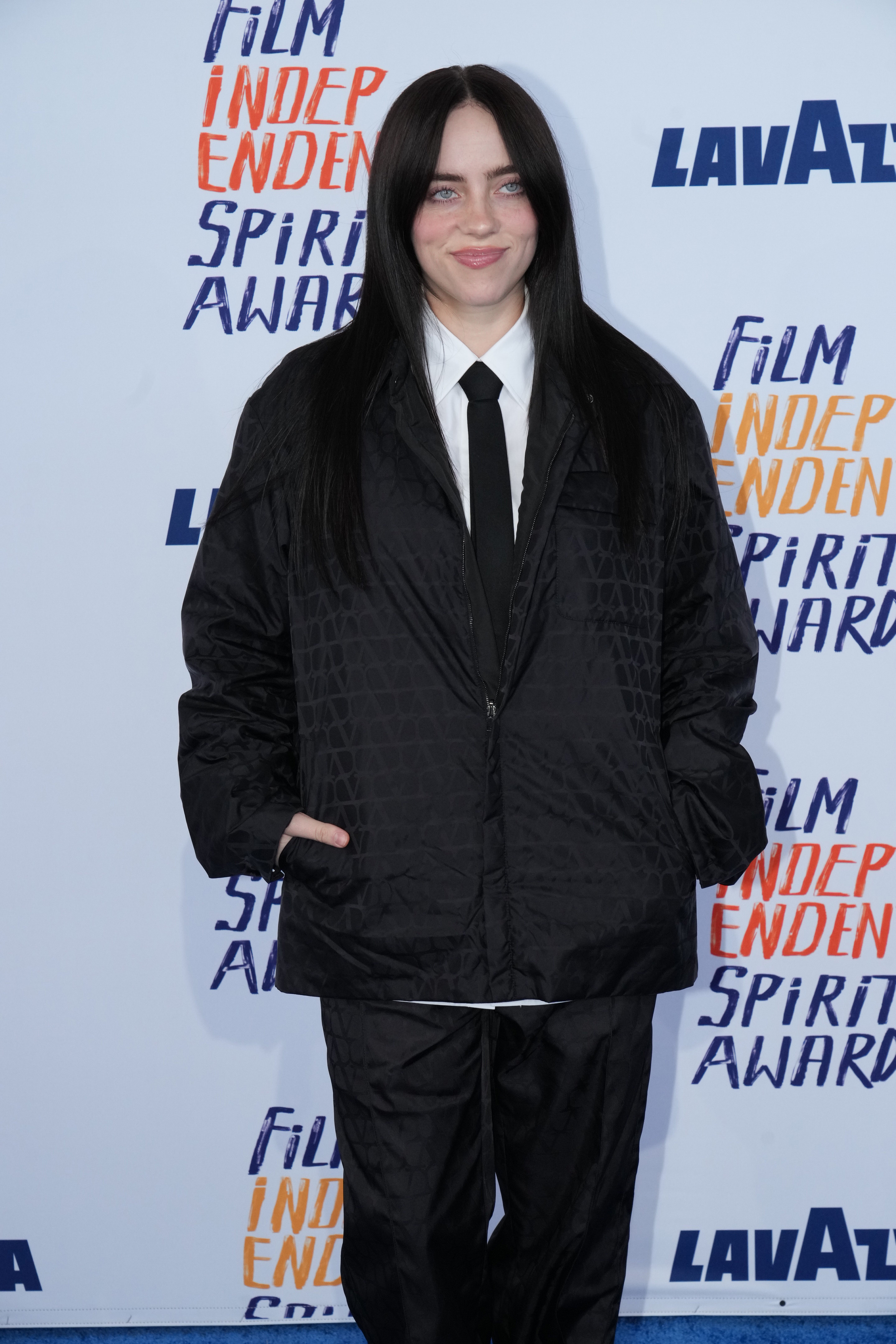Billie Eilish on a backdrop, wearing an oversized patterned jacket and pants with hands in pockets