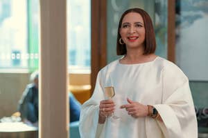 Maya Rudolph in elegant white dress holding a champagne flute, smiling at an event