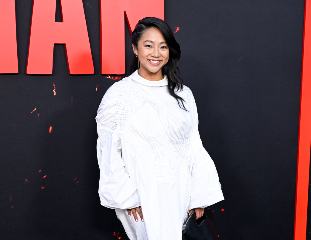Stephanie in an oversized blouse and trousers posing at an event with a promotional background
