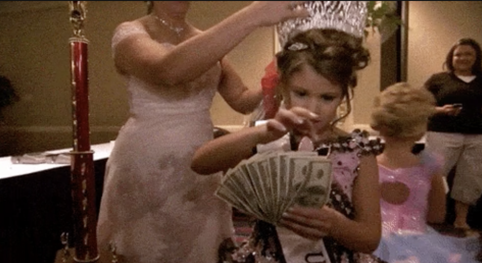 Young pageant winner holding cash with adult behind