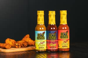 Three "Hot Ones" hot sauce bottles lined up next to a plate of chicken wings