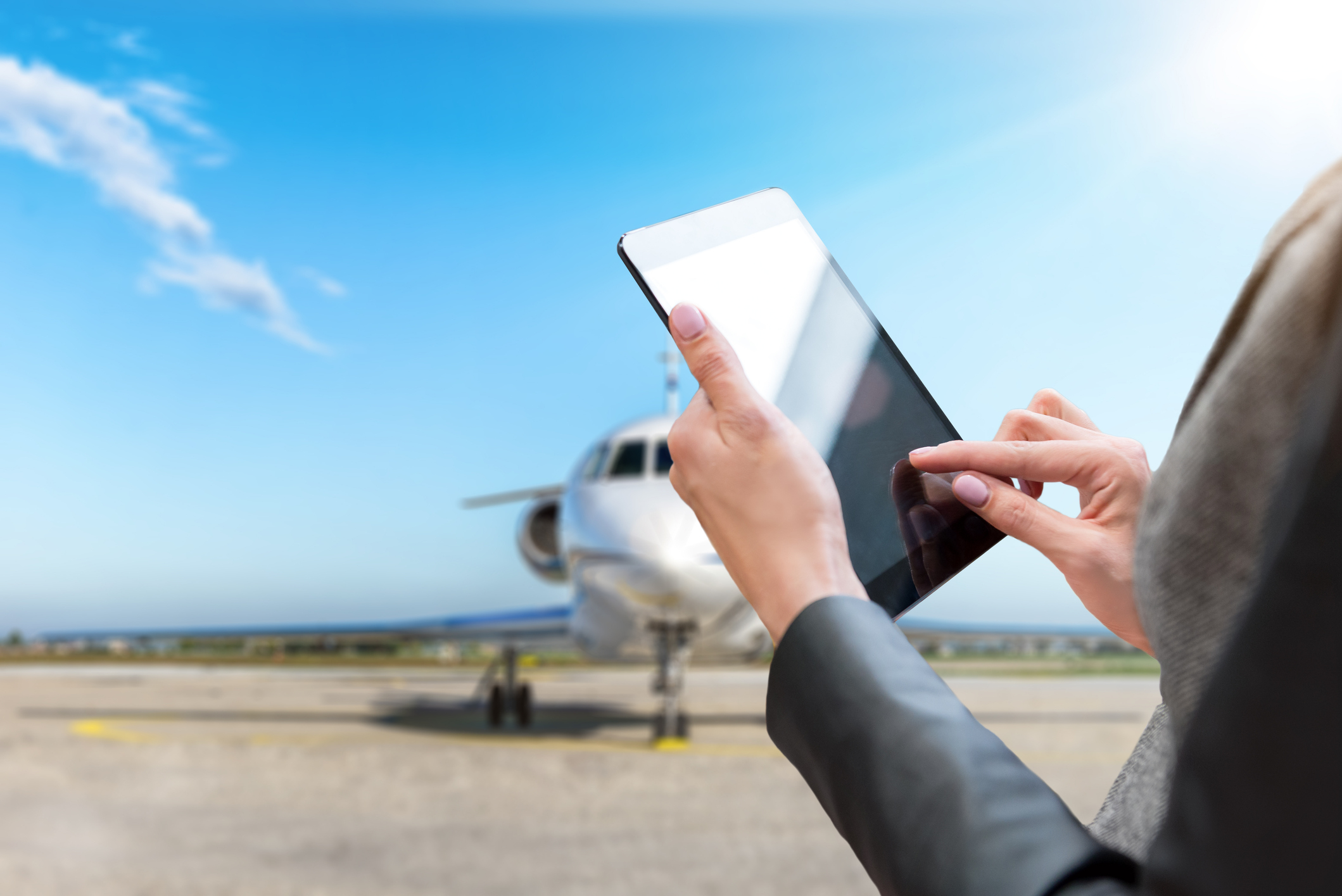 Person using a tablet with a private jet in the background, highlighting luxury work travel