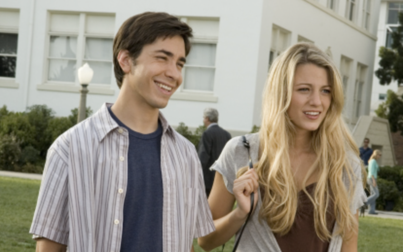 Two actors playing characters walking and smiling. Woman has long hair, man in striped shirt. They appear to be in a film scene