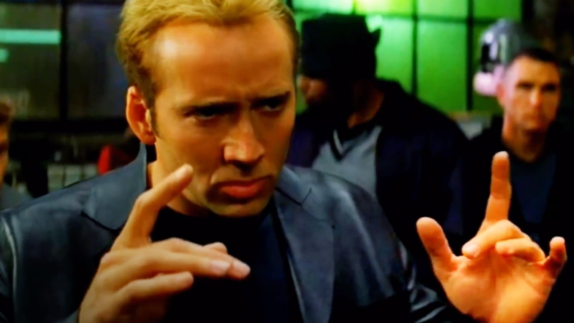 Nicolas Cage making a hand gesture as if explaining something, in a scene from a movie