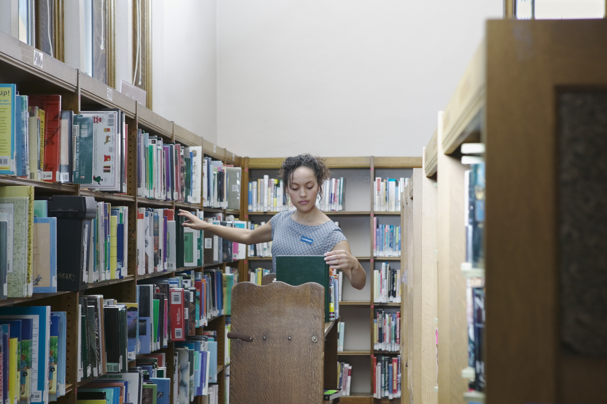 A person browsing books on library shelves, selecting one to examine