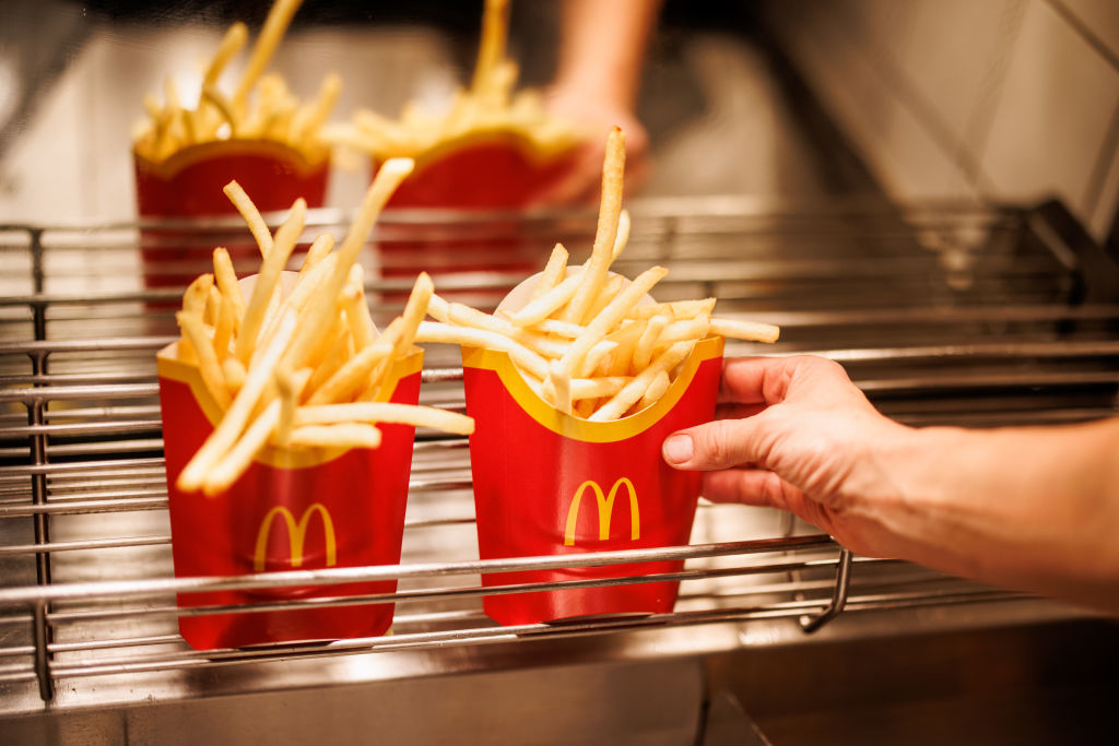 Person holding two containers of McDonald&#x27;s fries over a metal tray