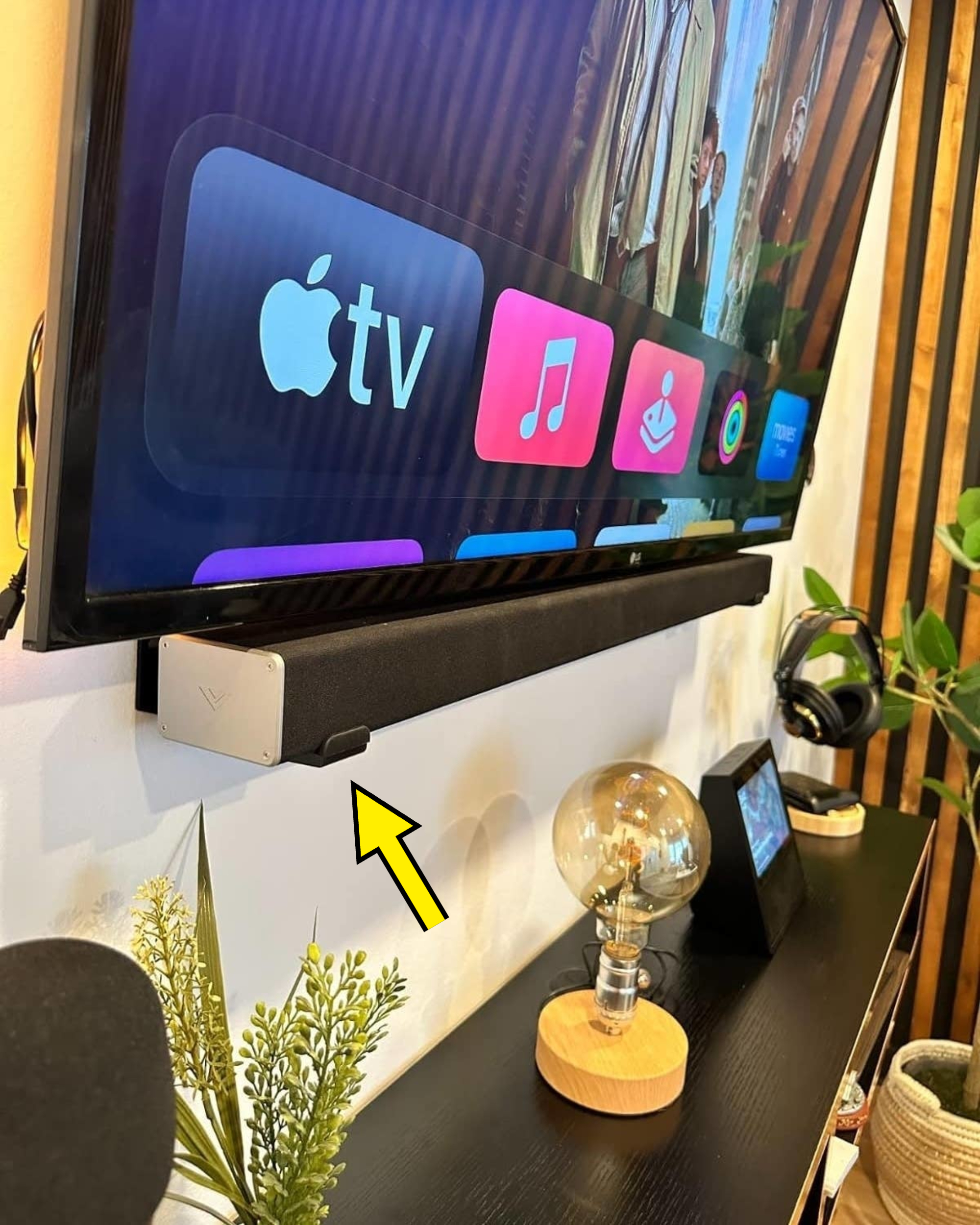 TV mounted on wall displaying Apple TV interface, with soundbar and decorative items on the shelf below