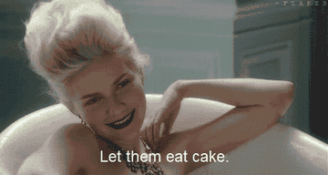 Mujer con labios oscuros sonríe en una bañera; parodia histórica, texto &quot;Let them eat cake&quot;