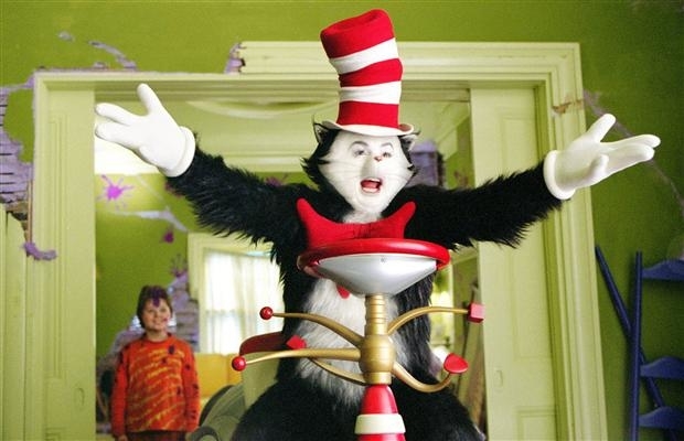 The Cat in the Hat character with a boy in the background. Cat is in costume with a tall striped hat and red bow tie, arms open wide