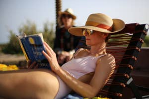 Tilda Swinton reading a book in a beach chair wearing a floppy hat.