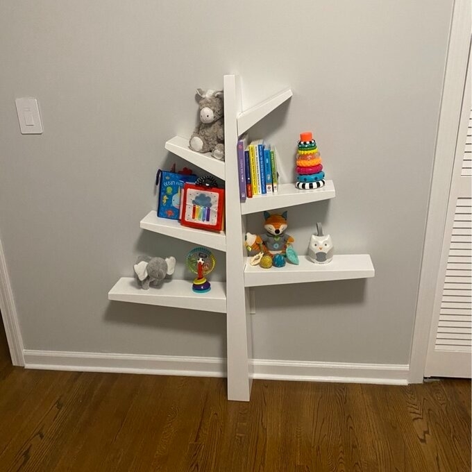 A corner wall shelf with various children&#x27;s items, including books, toys, and stuffed animals