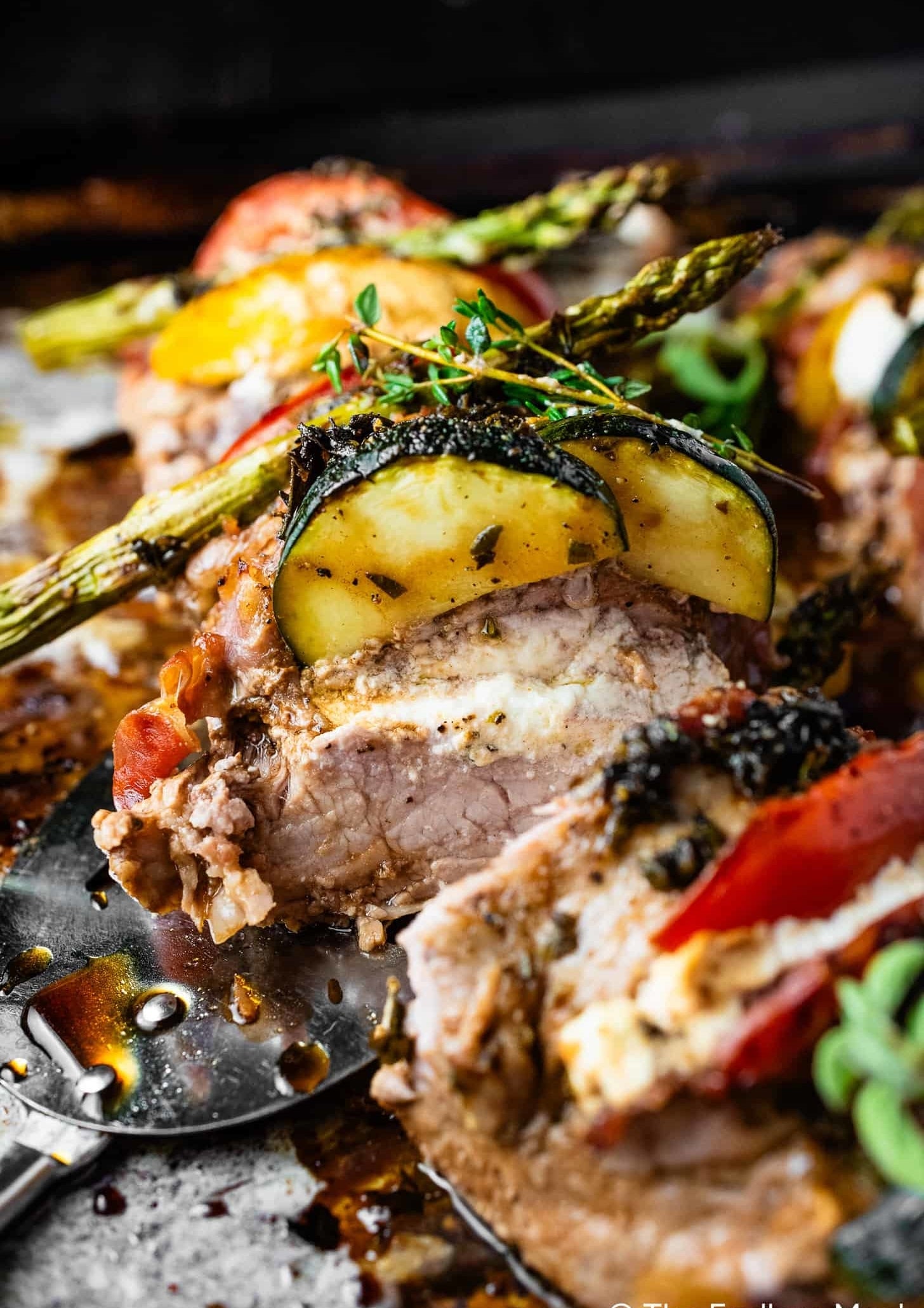 Grilled pork topped with zucchini and asparagus, fresh herbs on the side, on a rustic metal spatula