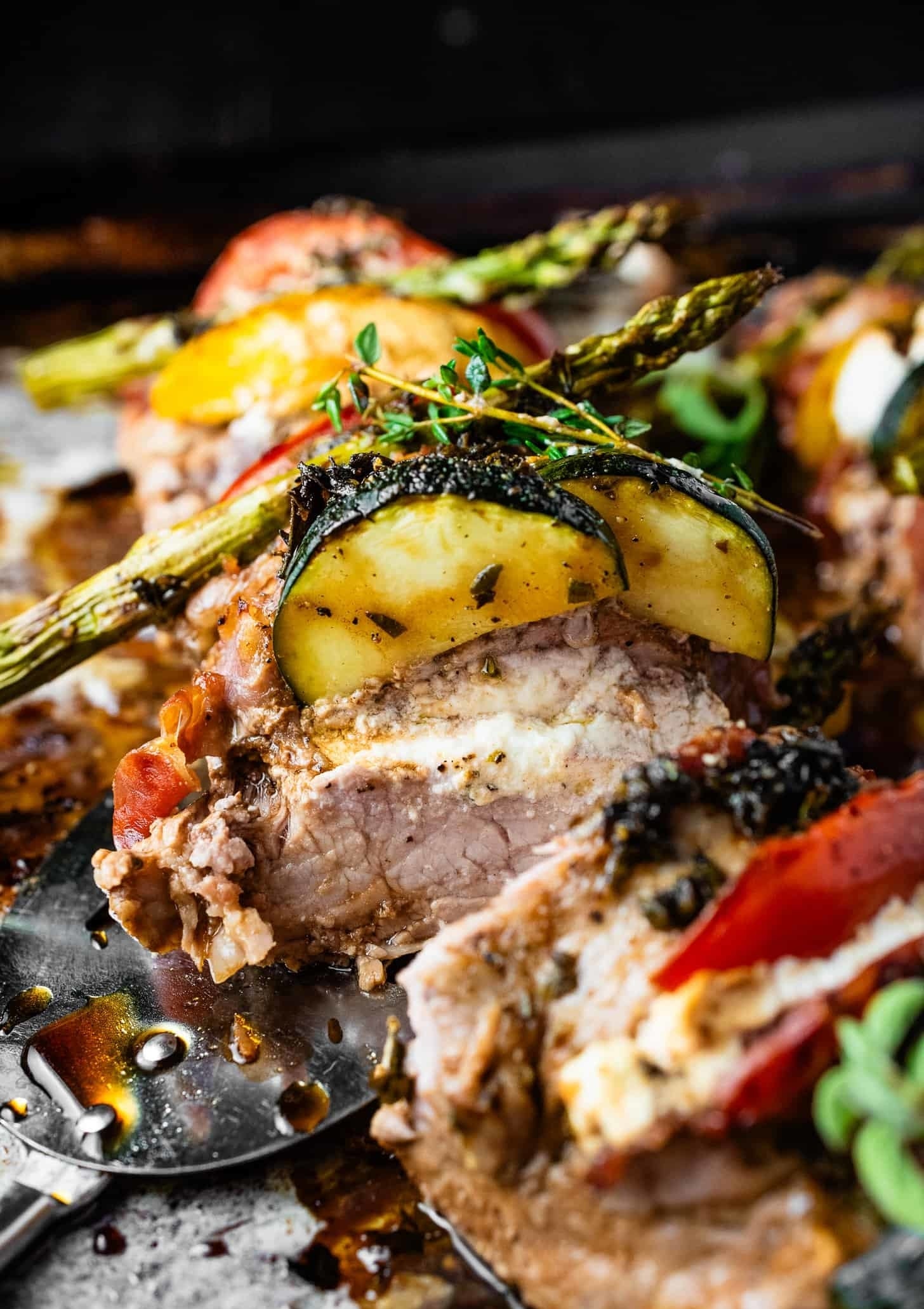 Grilled pork topped with zucchini and asparagus, fresh herbs on the side, on a rustic metal spatula