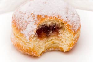 A close up of a jelly filled donut with a dusting of powdered sugar and a visible bite taken out