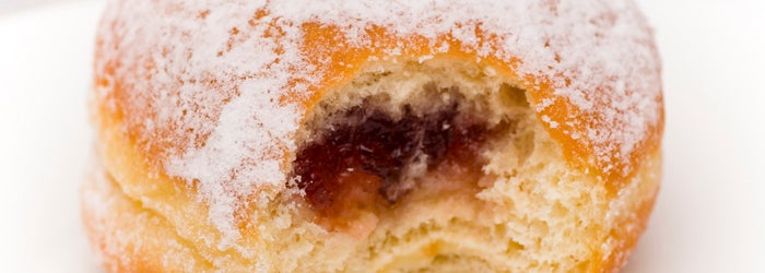 A close up of a jelly filled donut with a dusting of powdered sugar and a visible bite taken out