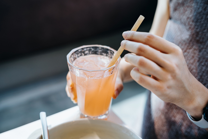 Close-up of a person&#x27;s hands holding a glass of juice with a straw