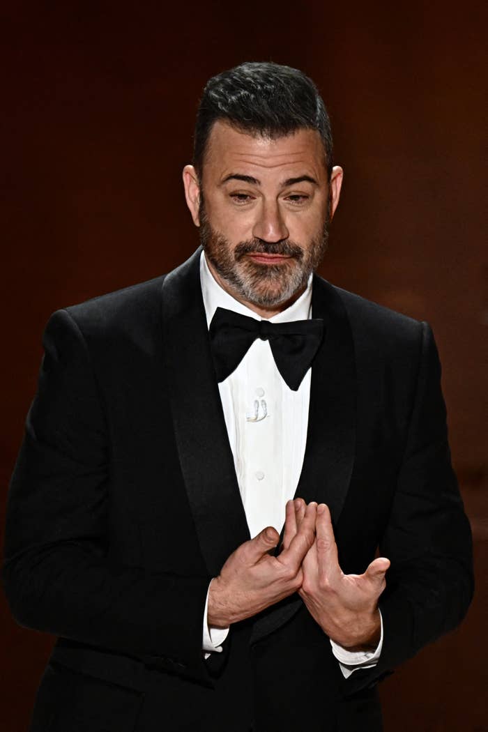 Jimmy Kimmel in a classic tuxedo, bow tie, hands clasped, at an event