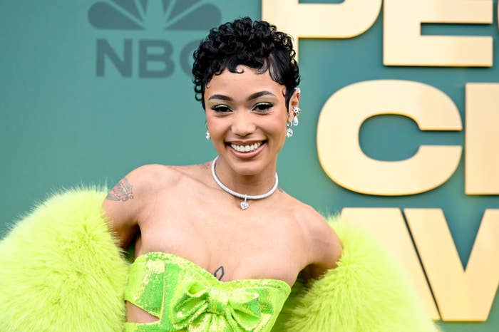 Coi Leray in green feathery outfit with bow detail, smiling at music event