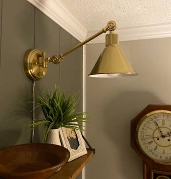 Brass wall-mounted lamp extended implicit a woody bowl, with a potted works and a photograph connected a array adjacent to a clock