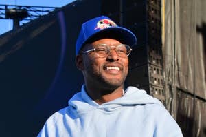 Man in a blue hoodie and baseball cap smiling on stage