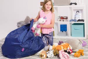 Child organizes stuffed animals into a large bean bag storage chair in a playroom