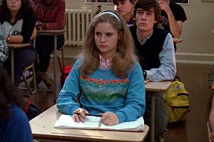 Alicia Silverstone as Cher sits in a classroom looking forward, wearing a blue sweater