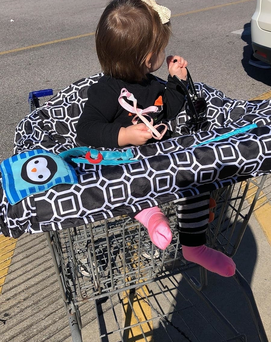Toddler in shopping cart with visible toy and blanket, playing with sunglasses