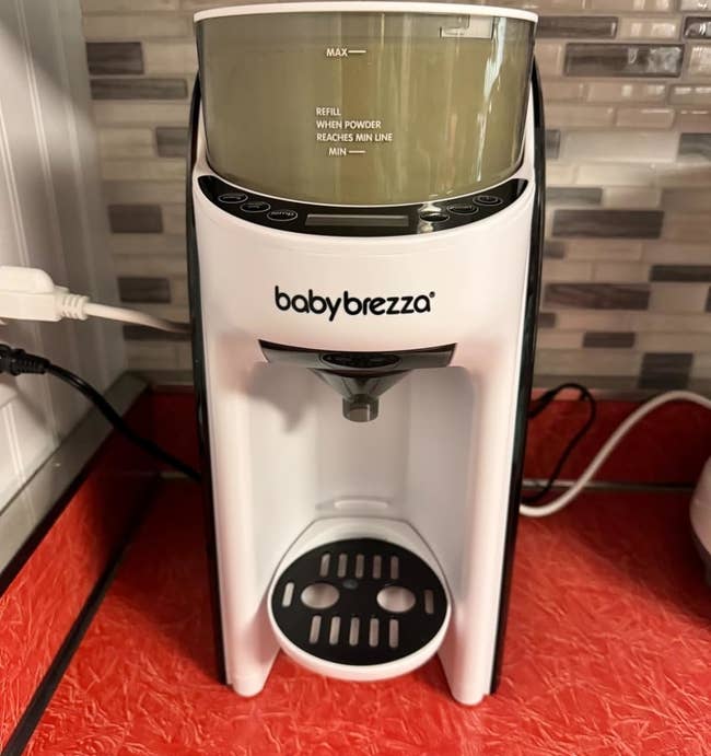 A reviewer's Baby Brezza appliance on a counter, used for making baby formula