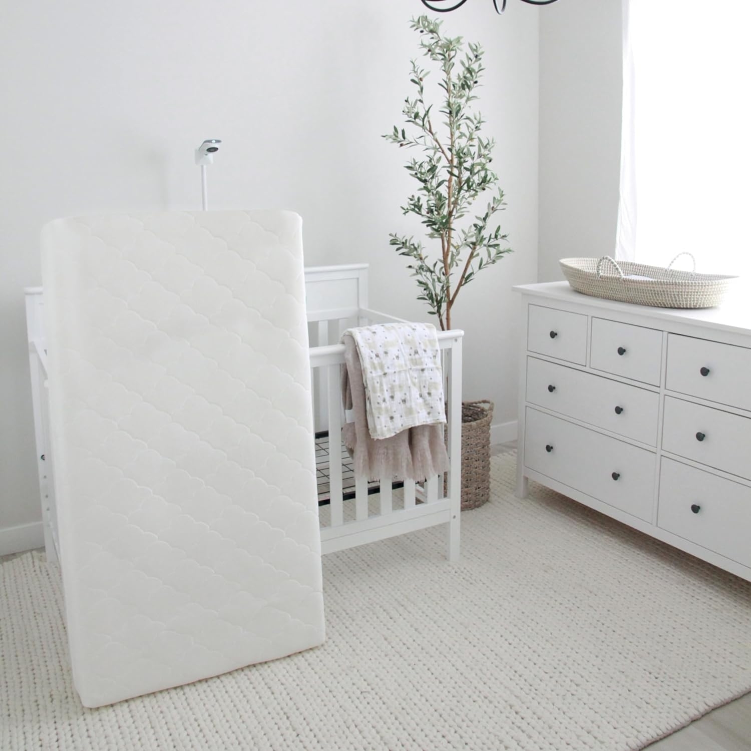 A crib mattress leaning against a wall next to a white crib and dresser in a nursery