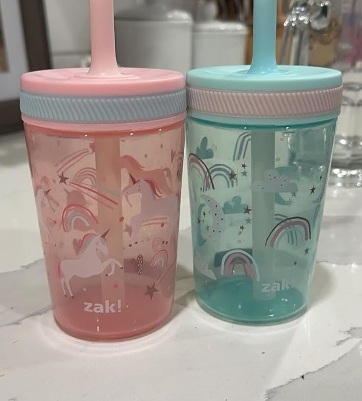 Two Zak! brand toddler cups with sippy lids, one pink with unicorns, one blue with rainbows