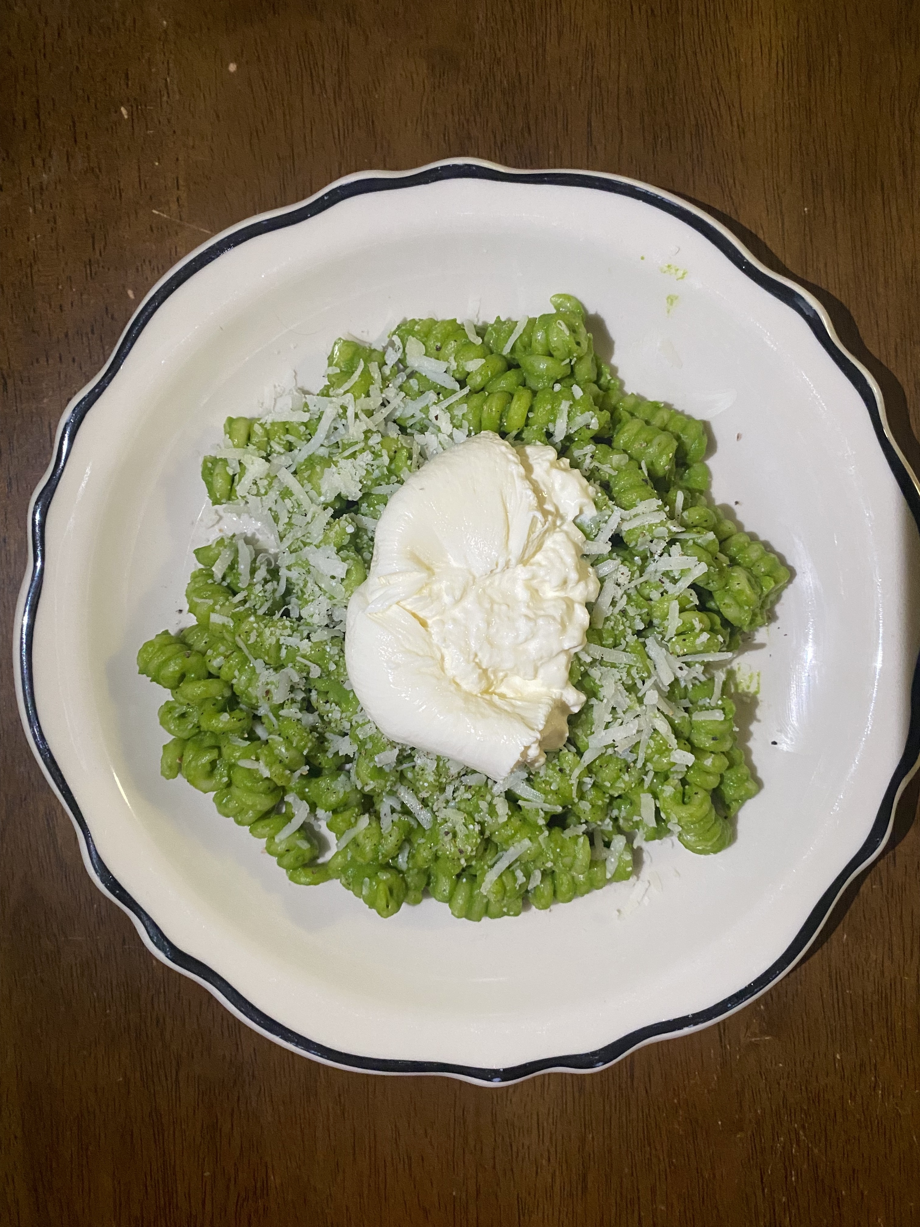 Plate of green pasta with cheese and a dollop of burrata on top
