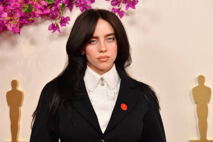 Billie Eilish in a black suit with an oversized jacket, white shirt, and a red lapel accent