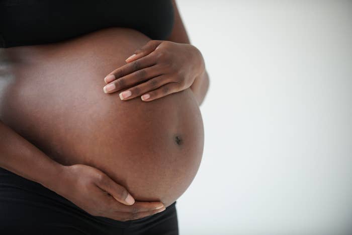 Close-up of a pregnant person gently cradling their belly with both hands