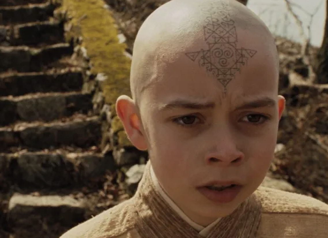 Character Aang with arrow tattoo on his bald head looking concerned outdoors