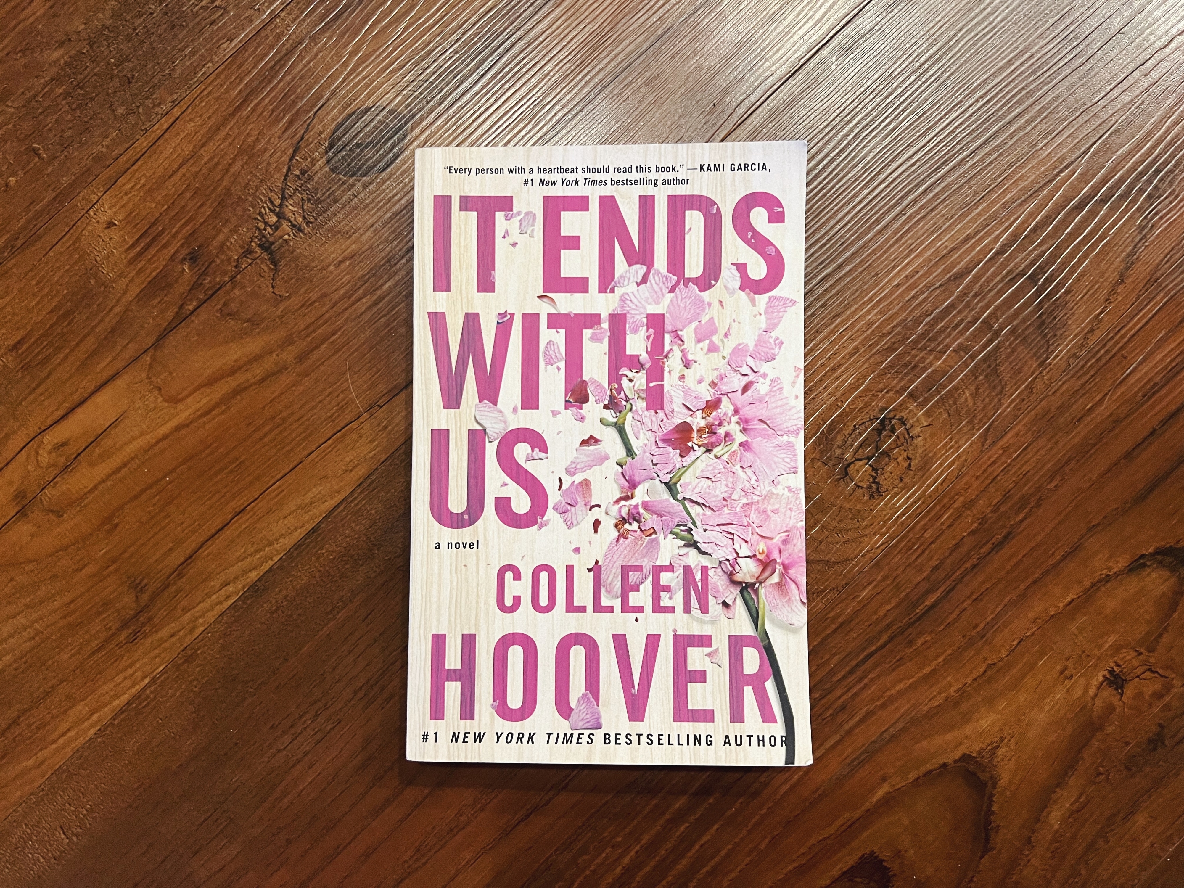 The image shows the book &#x27;It Ends With Us&#x27; by Colleen Hoover lying on a wooden surface