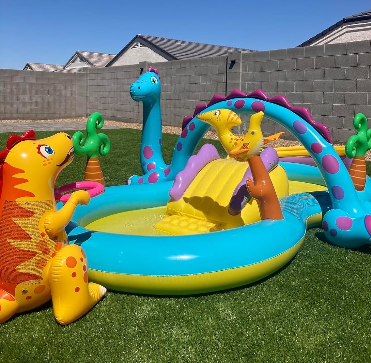 Inflatable dinosaur-themed children's pool with sprinkler and slide in a backyard