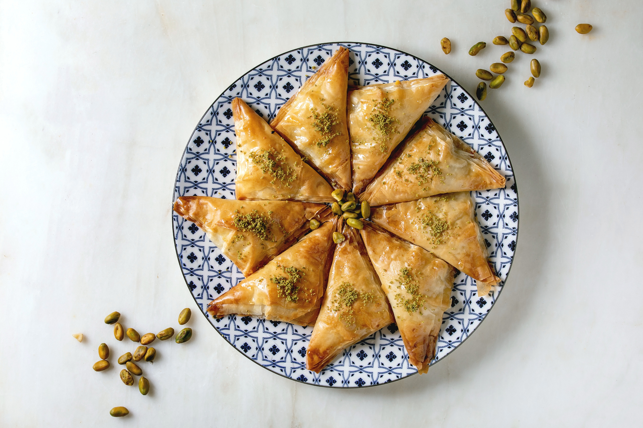 A plate of triangular pastries arranged in a star pattern, garnished with pistachios